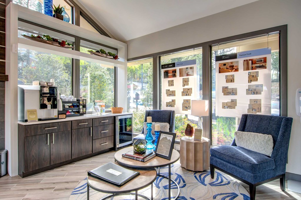 a living room with blue chairs and a coffee bar and large windows