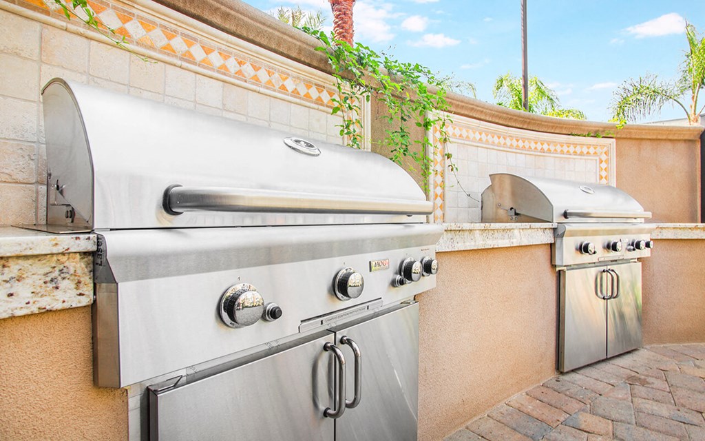 a stainless steel barbecue grill next to a wall with two stainless steel ovens
