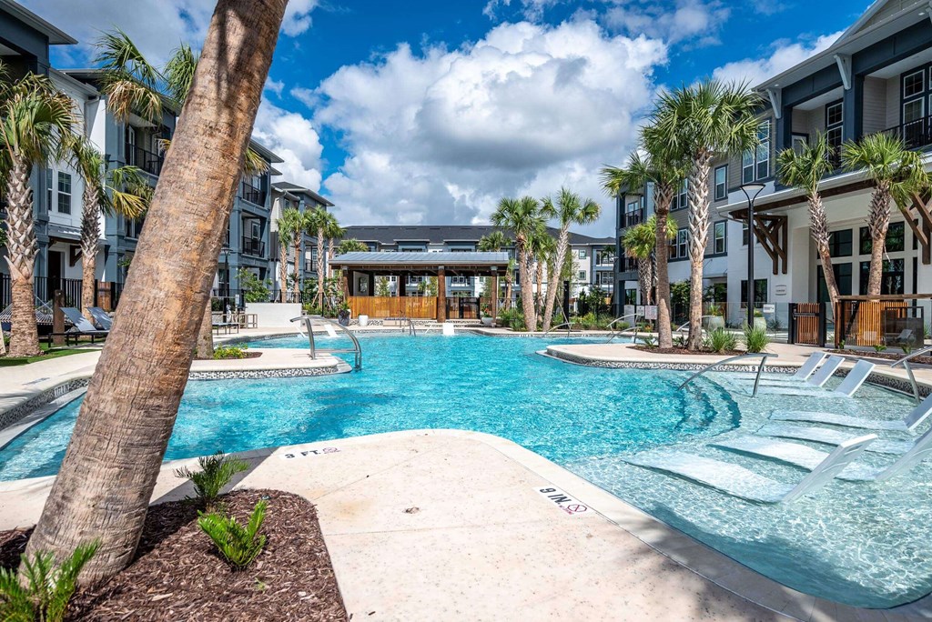a large swimming pool with palm trees and apartments in the background