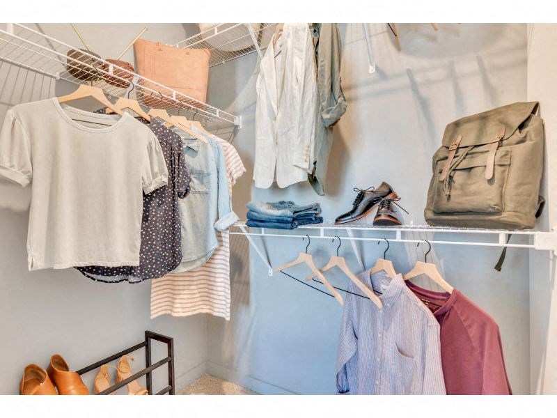 a closet with a rack of clothes and shoes and a backpack