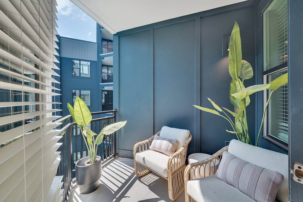 a small balcony with two wicker chairs and a plant
