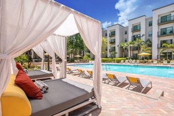 a swimming pool with chaise lounge chairs and a poolside cabana with buildings