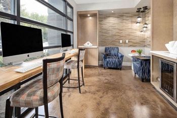 a room with a desk with a computer and chairs and a window