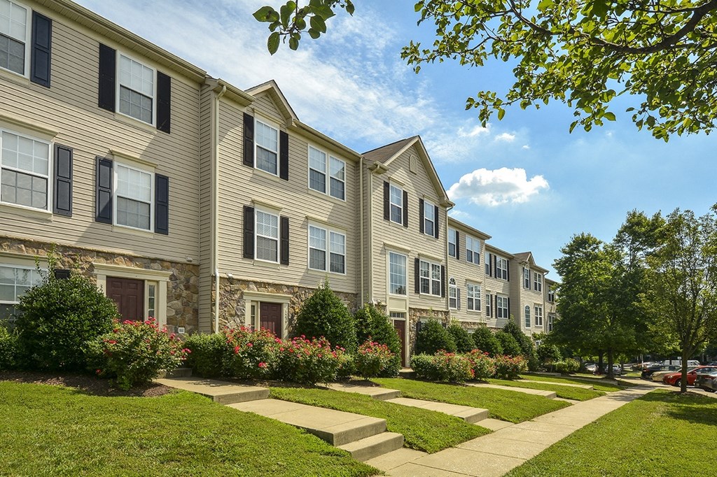 a row of apartment buildings with a sidewalk and landscaping