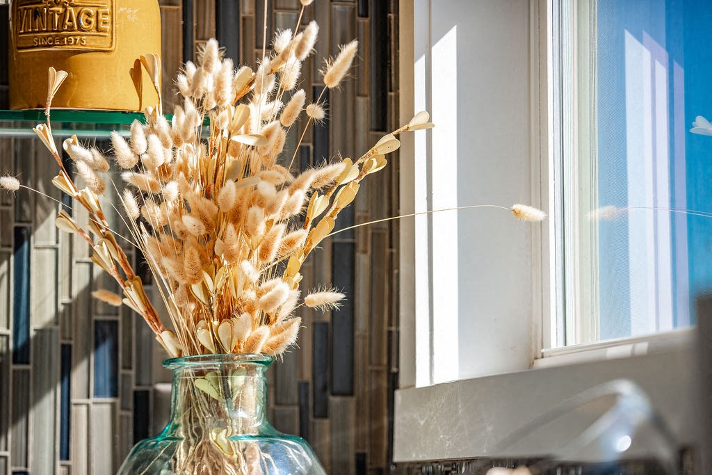 a glass vase filled with wheat in front of a window