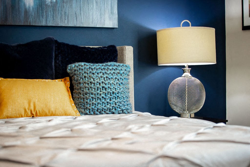 a bedroom with blue walls and a bed with pillows and a lamp