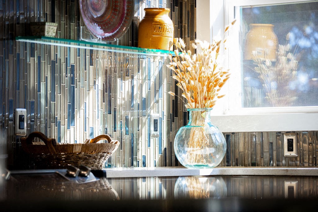 a glass vase with flowers on a counter next to a window