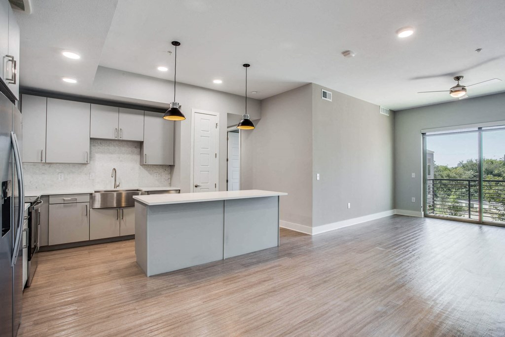 an empty living room with a kitchen and a window