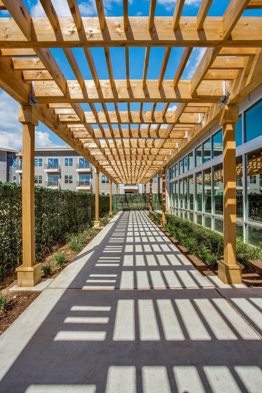 a long walkway under a wooden structure with shadows on the ground