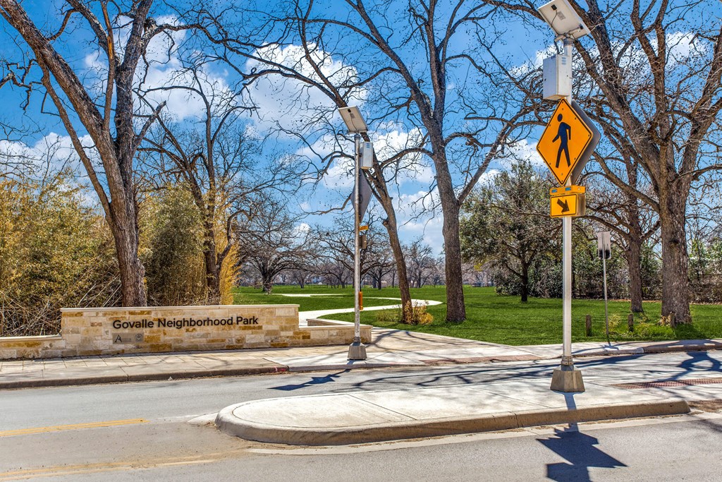 a street with a pedestrian crossing sign in front of a park