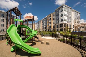 a playground with a green swing set in front of an apartment building