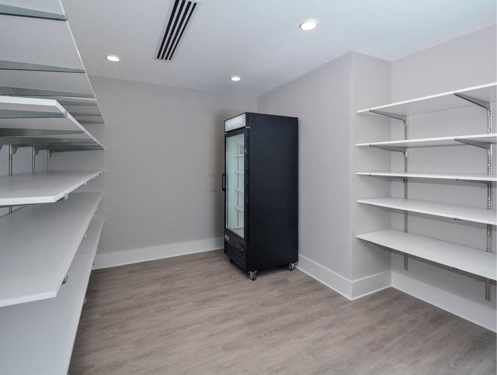 a large walk in closet with shelves and a black refrigerator