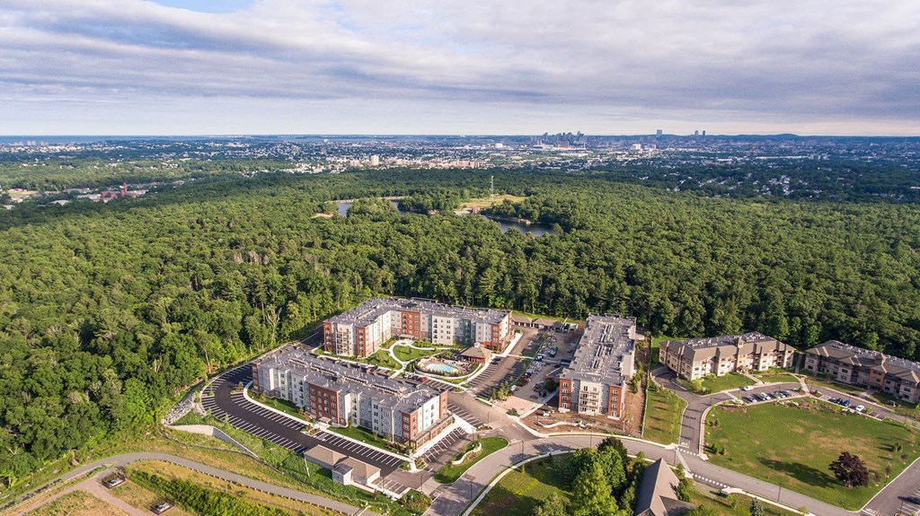 an aerial view of an apartment complex with trees and a city in the background