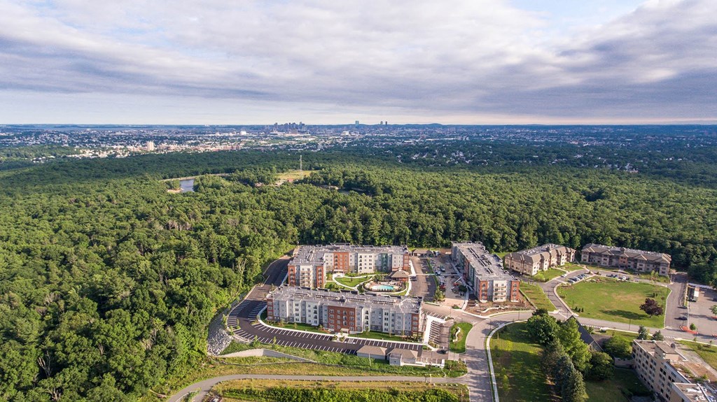 an aerial view of an apartment complex with trees and a city in the background