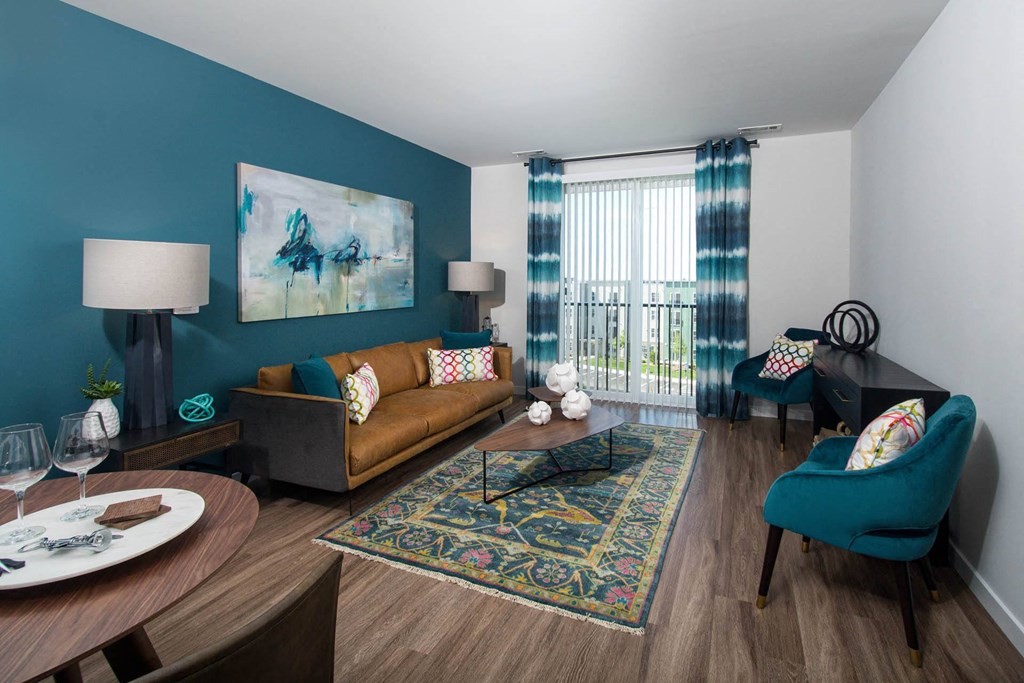 Model living room at Alta Clara apartments in Stoneham, MA, featuring wood grain flooring and a balcony.