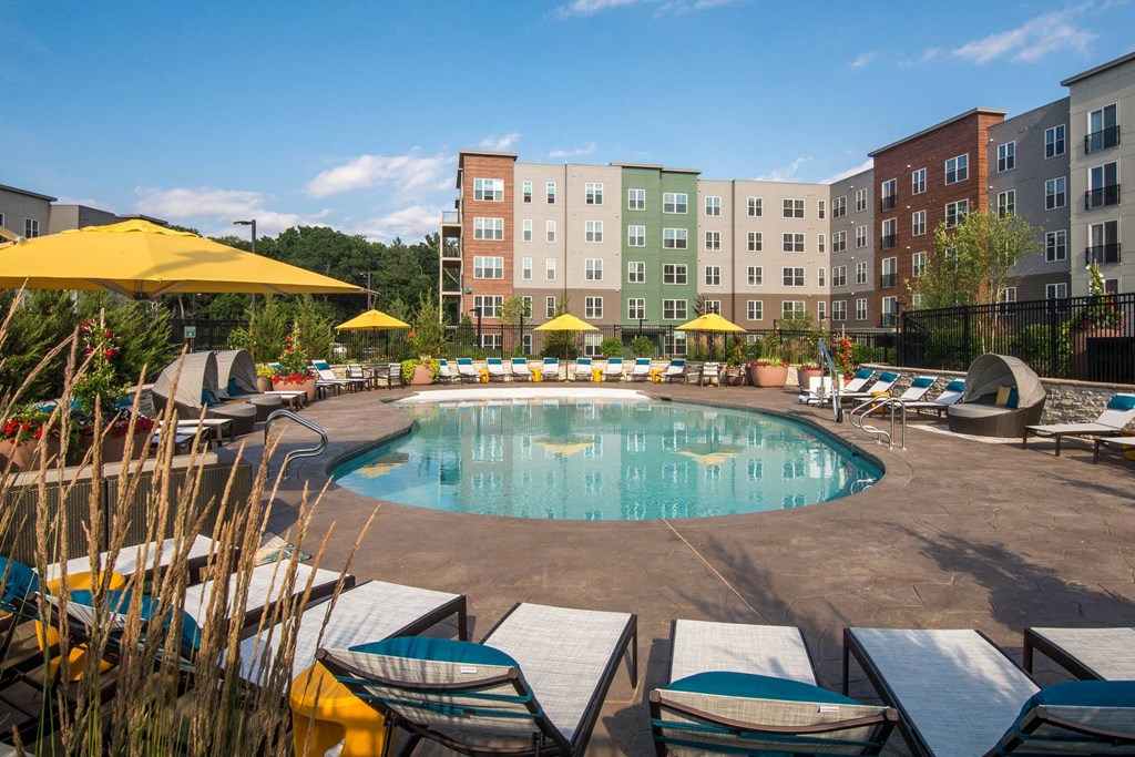 a swimming pool with chairs and umbrellas in front of an apartment building