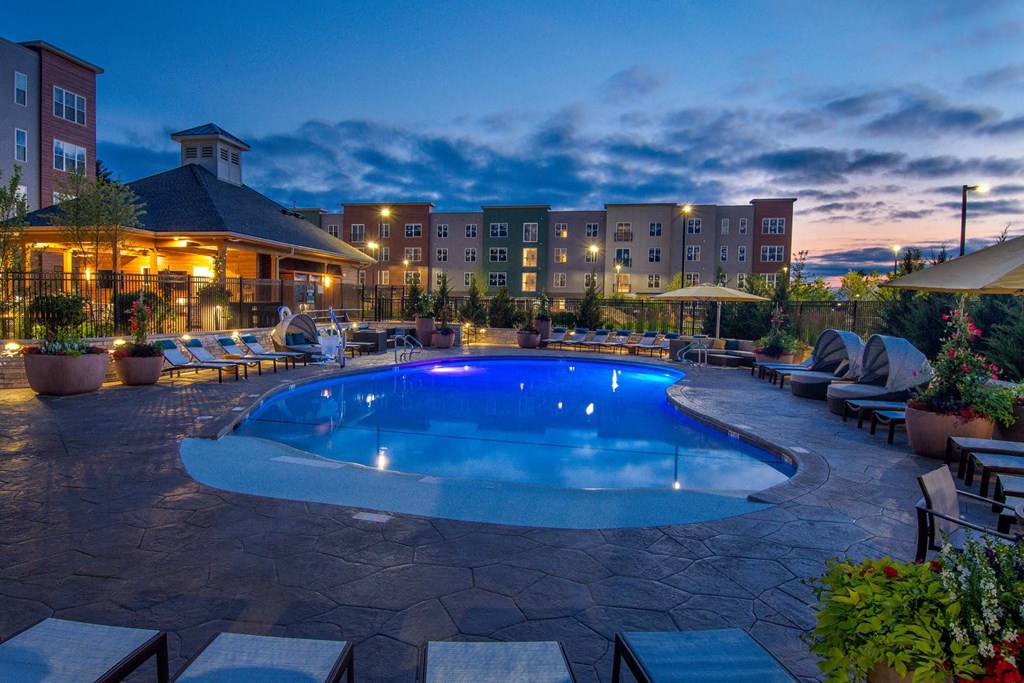 Outdoor swimming pool at Alta Clara apartments in Stoneham, MA, featuring lounge chairs and umbrellas.