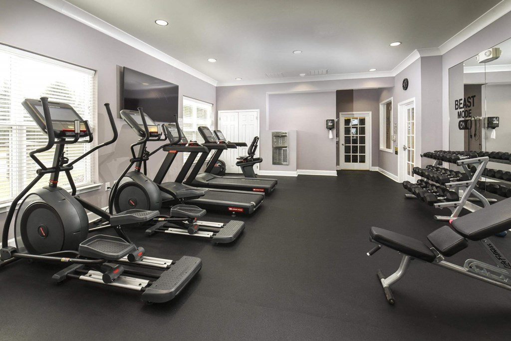 a gym with cardio equipment and a tv