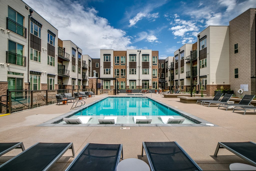 an apartment pool with lounge chairs in front of an apartment building