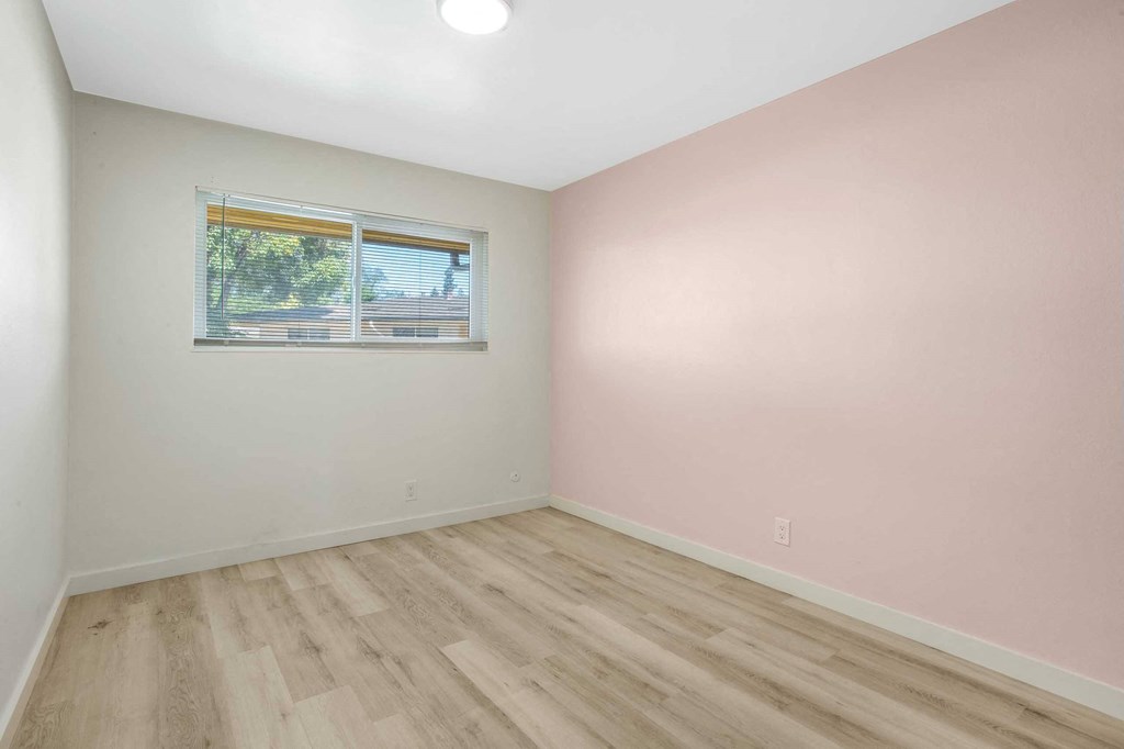 a bedroom with pink walls and wood floors and a window