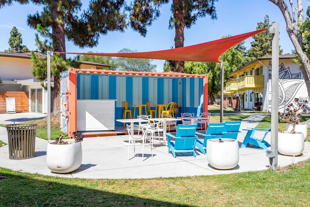 a patio with chairs and tables in front of a blue and orange building