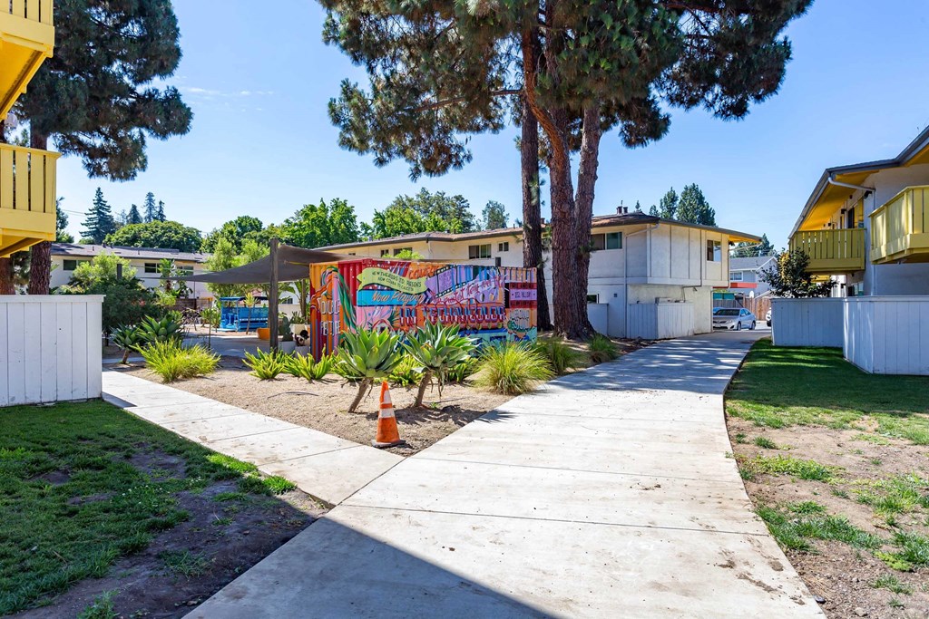 a sidewalk in front of a house with a colorful mural on the wall