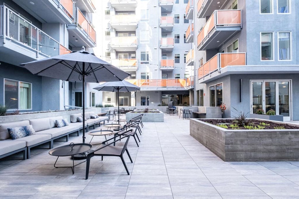 a patio with tables and umbrellas in front of an apartment building