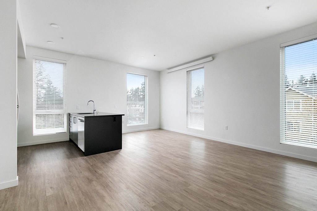 an empty living room with wood floors and a kitchen