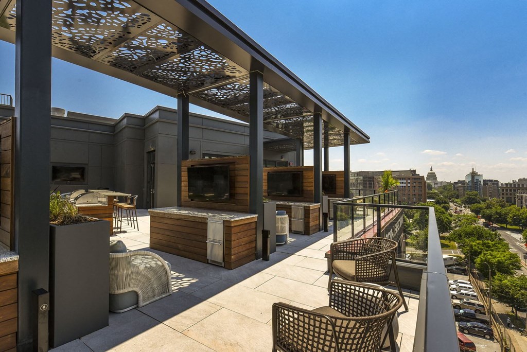 a rooftop patio with chairs and a tv and a building in the background
