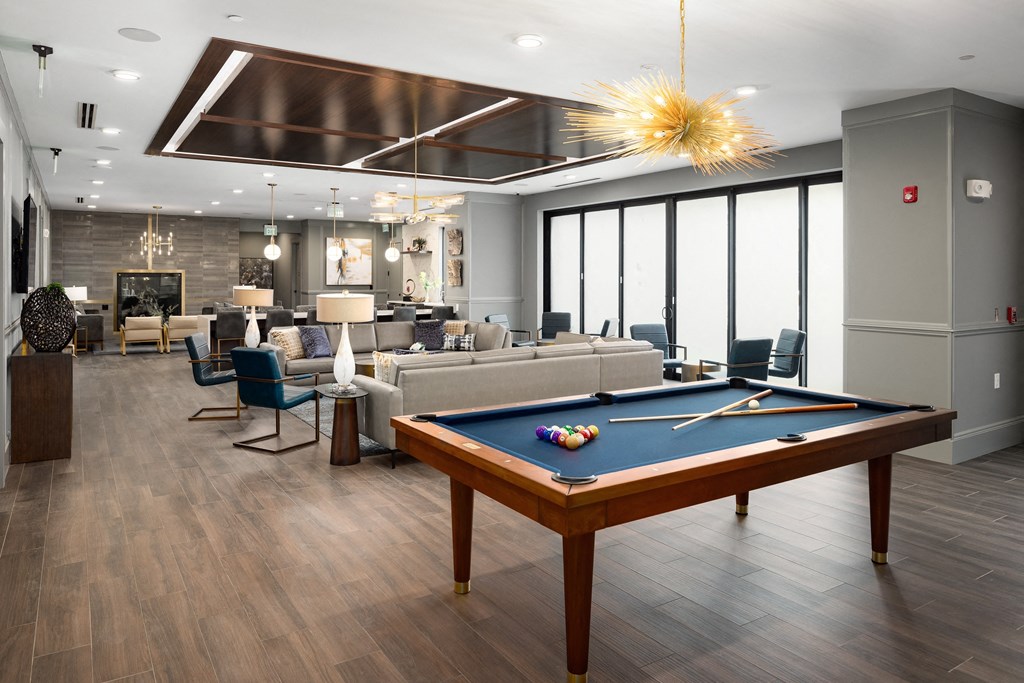 a community room with a pool table and couches and a living room with windows