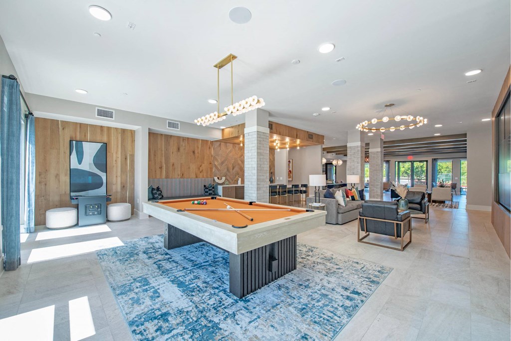 a pool table in the center of a clubhouse with couches and chairs