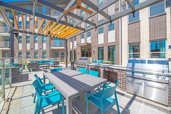 Covered outdoor kitchen area with outdoor TV, gas grill stations, fireplace with seating for lounging and dining