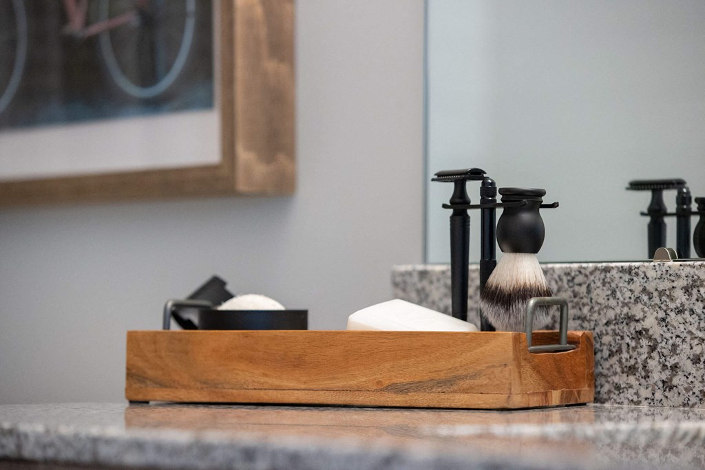 a bathroom sink with a wooden tray with a soap dispenser and a shaving brush