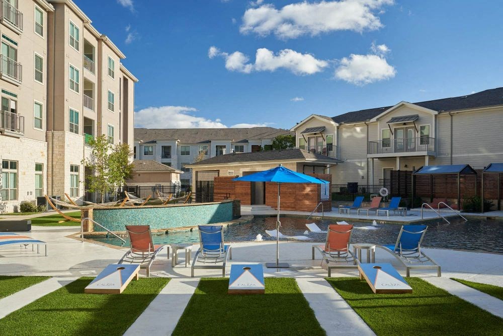 a swimming pool with chairs and umbrellas in front of an apartment building