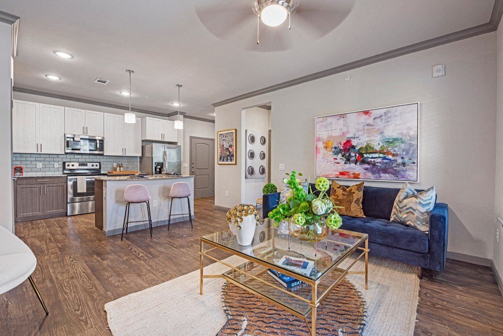 a living room with a glass coffee table and a kitchen in the background