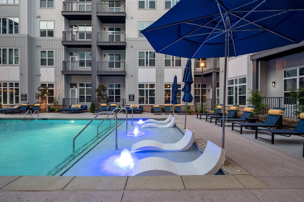a swimming pool with a blue umbrella and some chairs in front of an apartment building