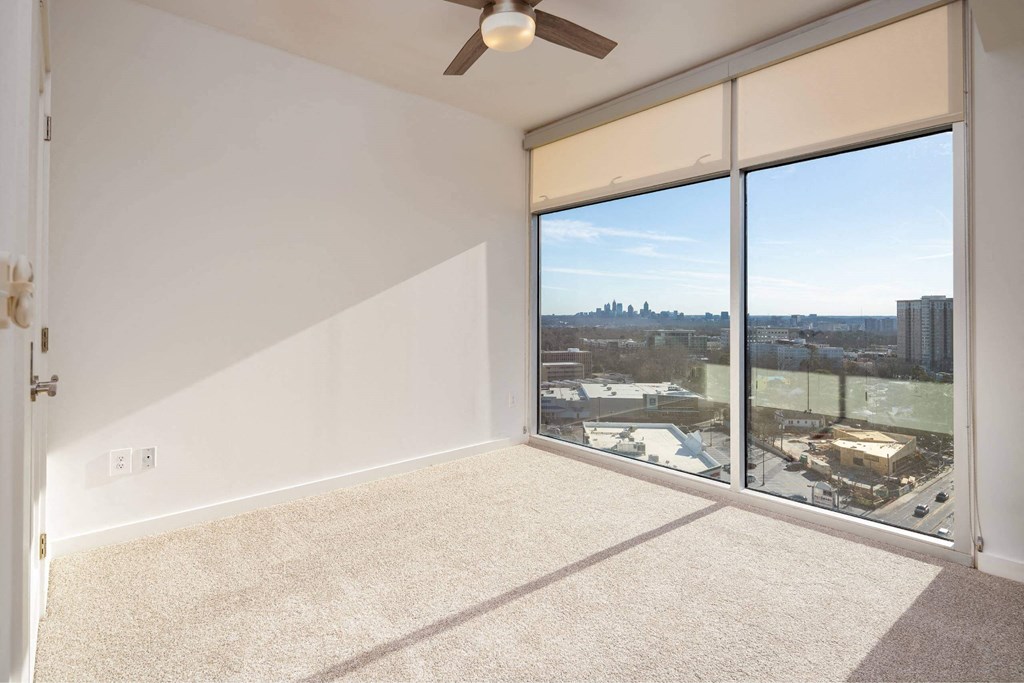 an empty living room with a large window and a ceiling fan