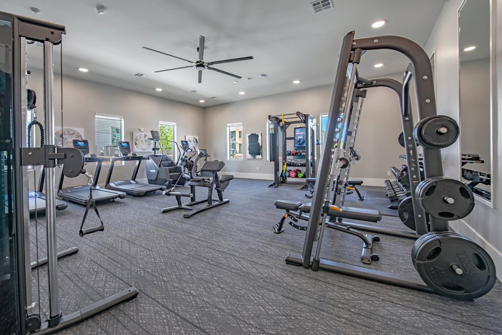 a gym with weights and cardio equipment and a ceiling fan