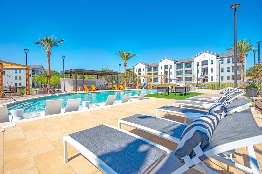 a pool with lounge chairs and a poolside building with apartments in the background