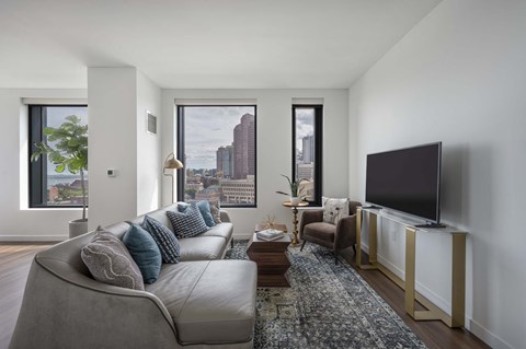 A living room with a grey couch and a large window overlooking the city.