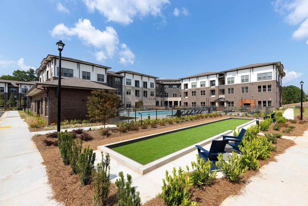 a courtyard with a lawn and chairs in front of an apartment building