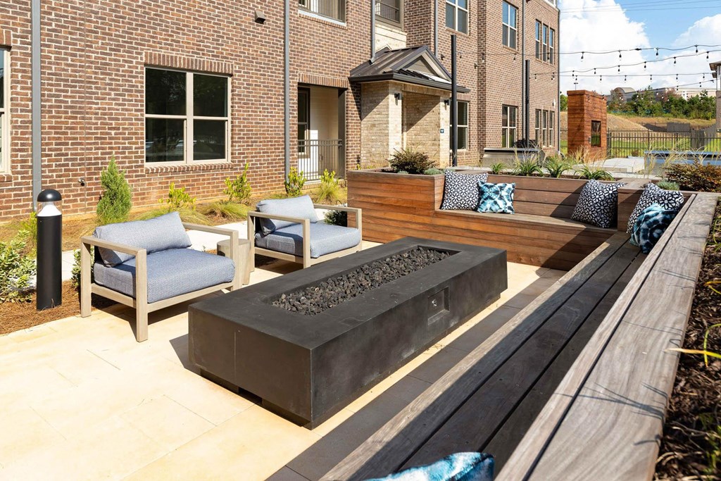 a patio with a firepit and furniture in front of a brick building
