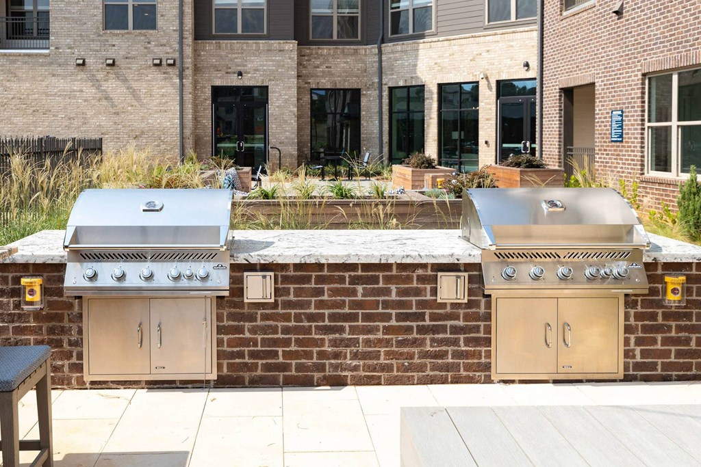 two stainless steel barbecue grills in front of a brick wall