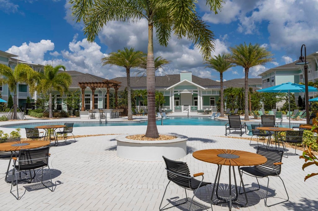 a swimming pool with tables and chairs and a house in the background