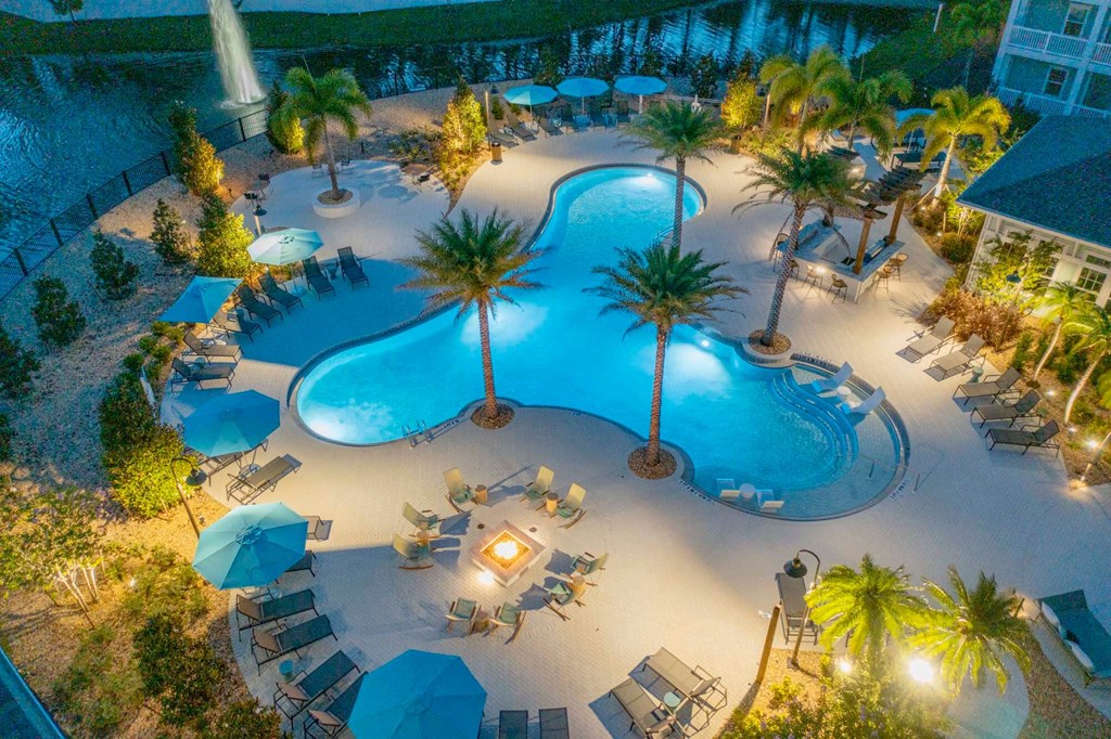 a resort style swimming pool with palm trees and umbrellas at night