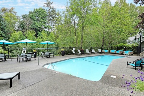 Outdoor pool with lounge chairs and turquoise umbrellas at Hidden River Townhomes Apartments, Washington, 98034