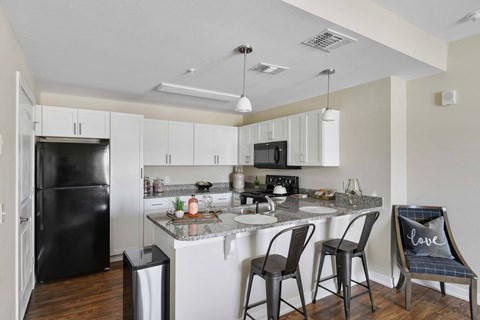 A kitchen with a black refrigerator and white cabinets.
