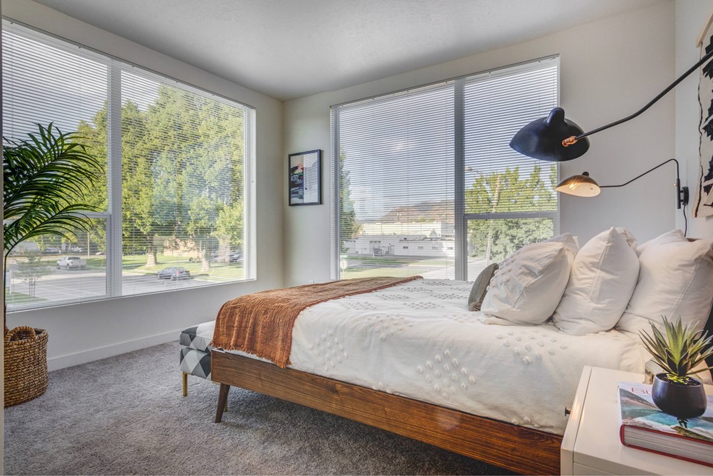 bedroom with large windows and a bed with white sheets and pillows