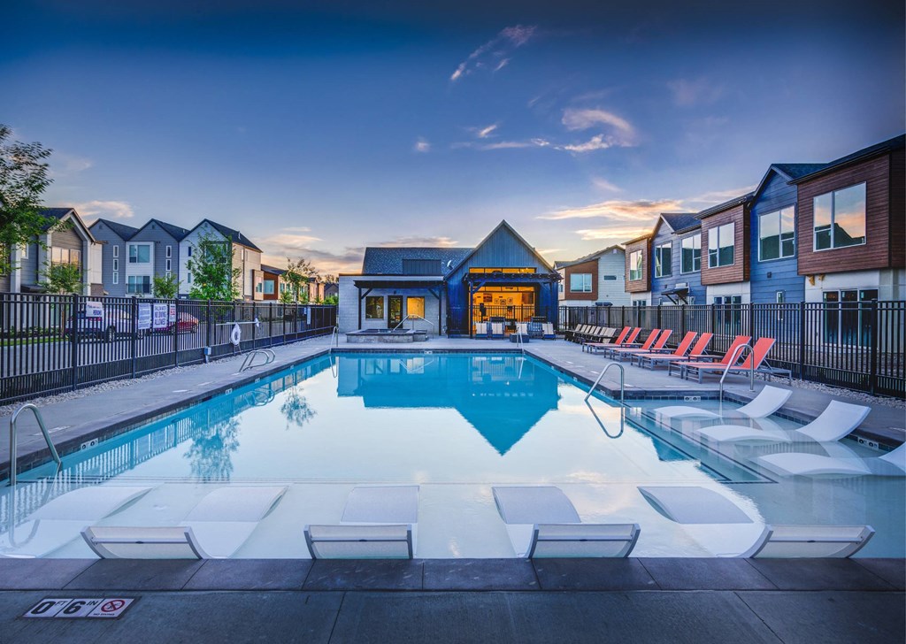 a swimming pool with chairs around it at dusk