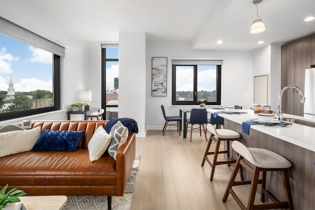 A modern living room with a brown leather couch and a kitchen area with bar stools.